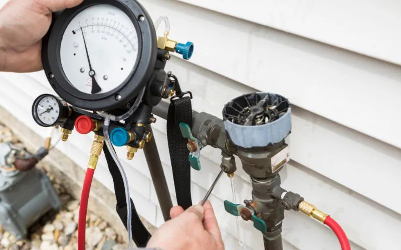 Certified plumber using differential pressure test gauge kit on test cocks of an exterior residential PVB backflow preventer
