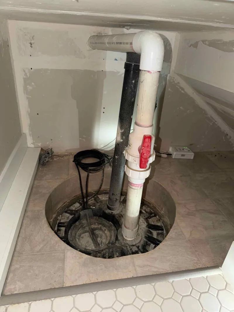 Basement closet sump pump pit with vertical PVC discharge pipe, red shutoff ball valve, and airtight radon cover