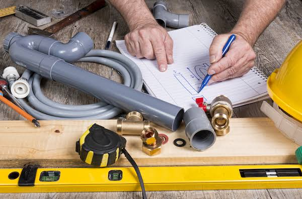Plumbing Engineer Reviewing Blueprint Schematics, PVC Fittings, Tape Measure and Brass Valves