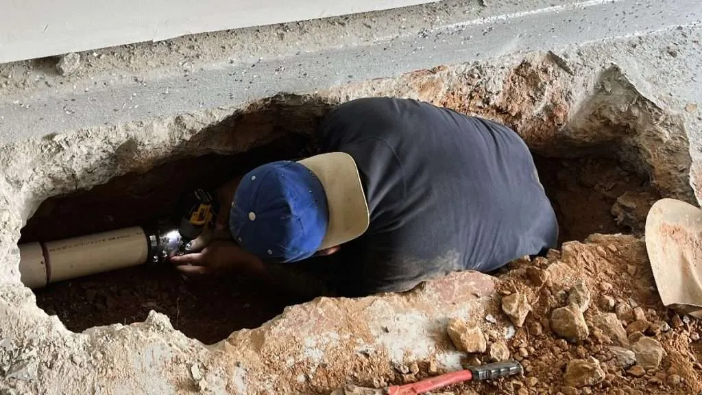 Plumber Working in Basement Slab Cutout Connecting New PVC Sewer Pipe with Heavy-Duty Couplings